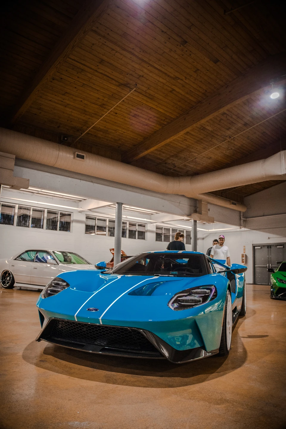 Bright blue supercar with white stripes under a wooden ceiling at an indoor car show