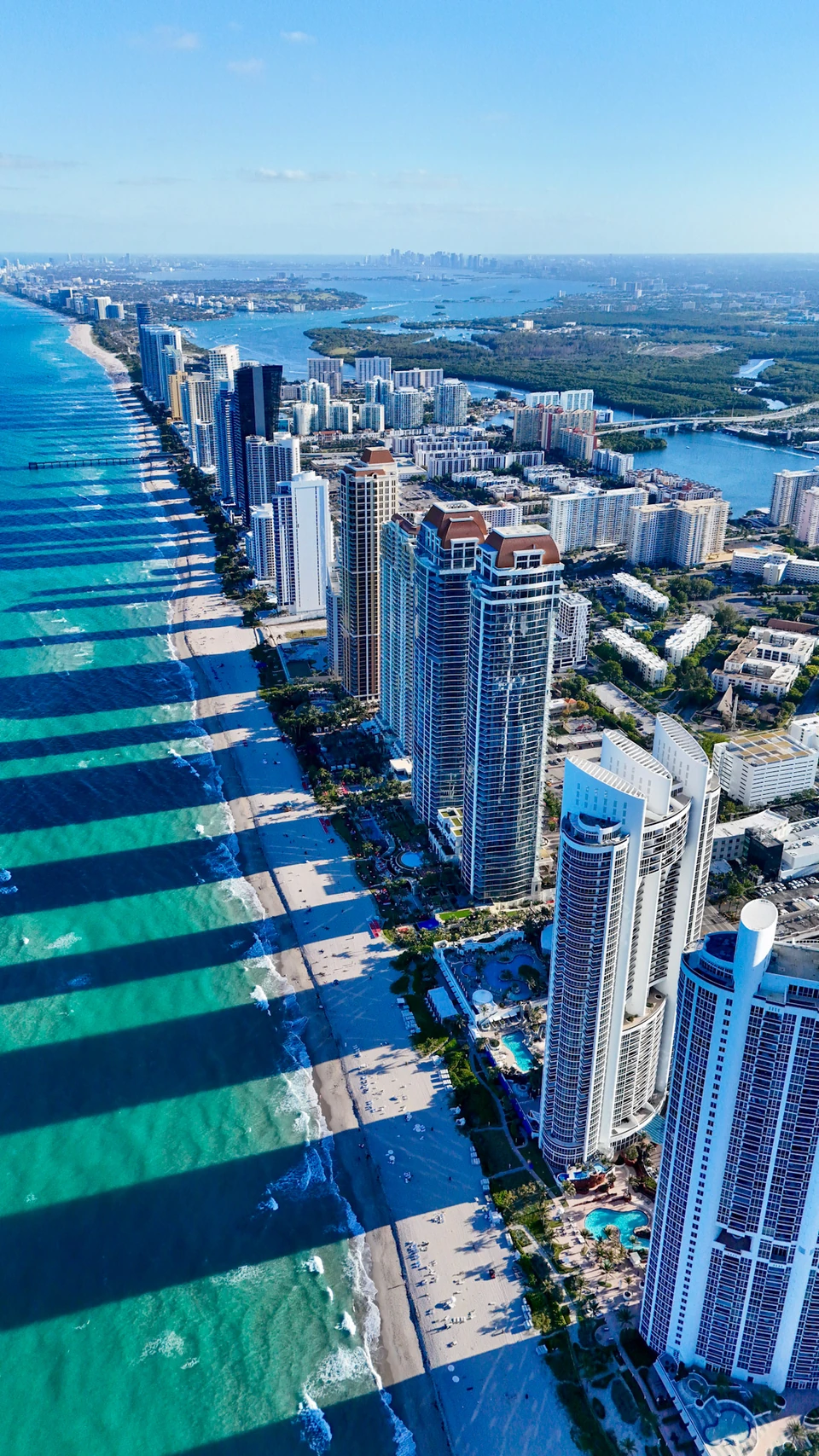 Aerial view of beachfront towers casting long shadows toward turquoise water
