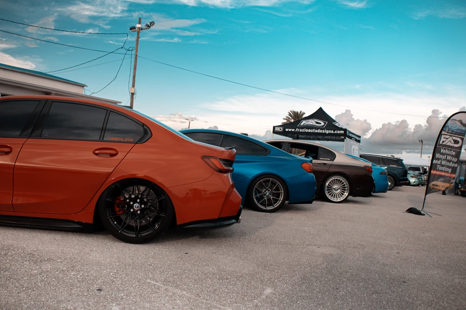 Row of BMW sedans in orange, blue and gray parked under a bright, partly cloudy sky