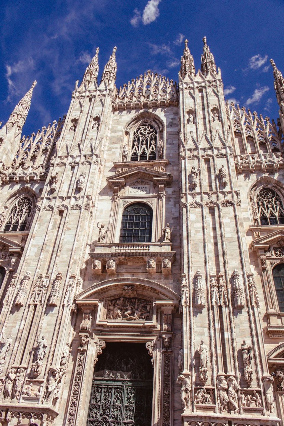 Looking up at the ornate white Gothic facade of a cathedral against a blue sky