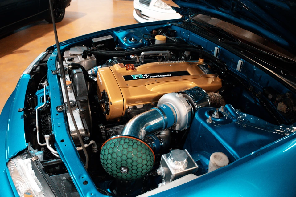 Close view of a gold-cammed straight-six engine with a turbo and green air filter in a bright blue engine bay