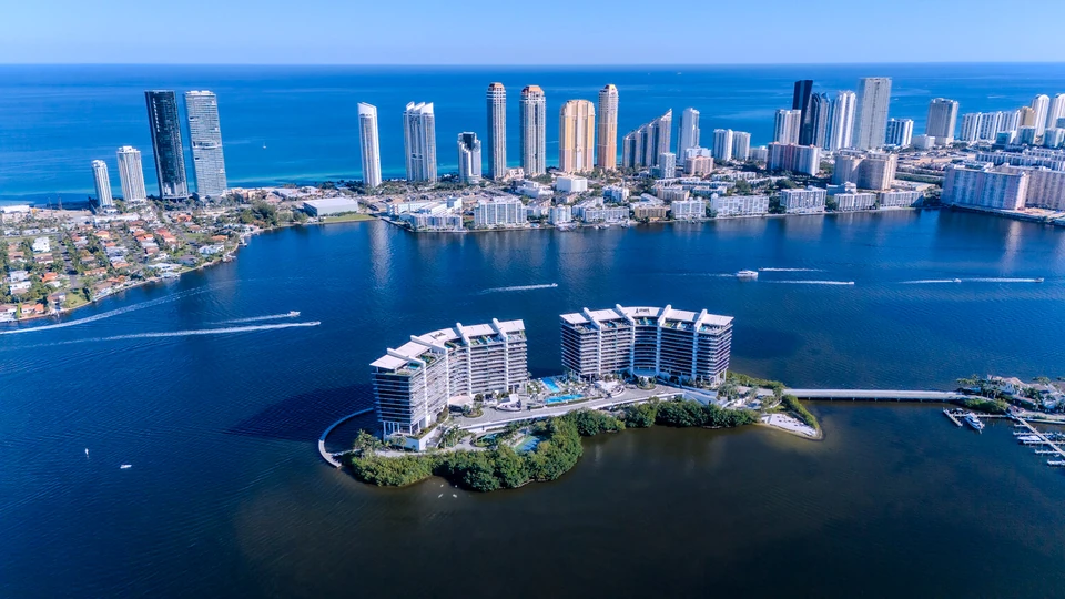 Aerial view of a small residential island with a line of waterfront towers behind it