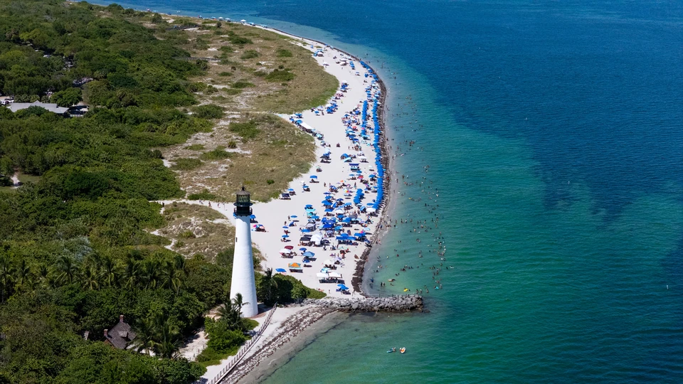 Aerial view of a white lighthouse beside a curved beach and turquoise water