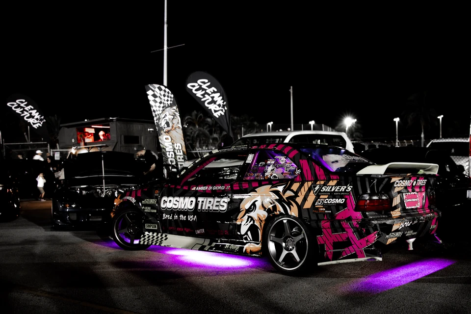 Drift-livery BMW coupe glowing with purple underglow at a nighttime car meet