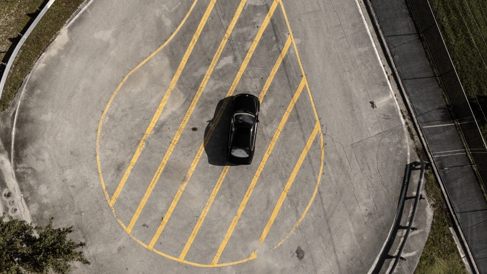 Top-down aerial view of a black sedan inside a teardrop of yellow painted lines on an empty lot