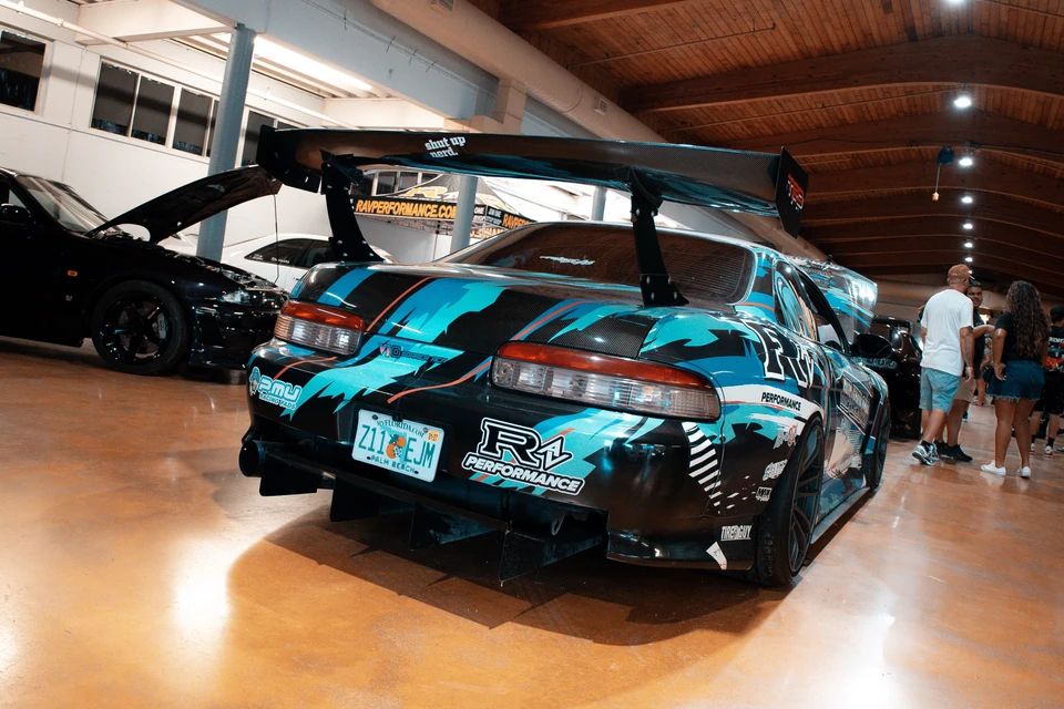 Rear of a liveried Toyota Supra with a tall rear wing on a polished indoor show floor